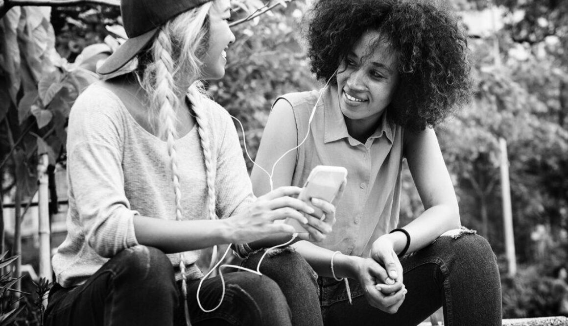 Young adult female friends listening to music through their smartphone outdoors