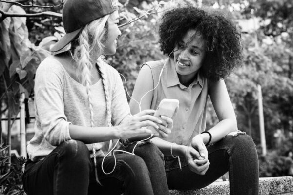 Young adult female friends listening to music through their smartphone outdoors